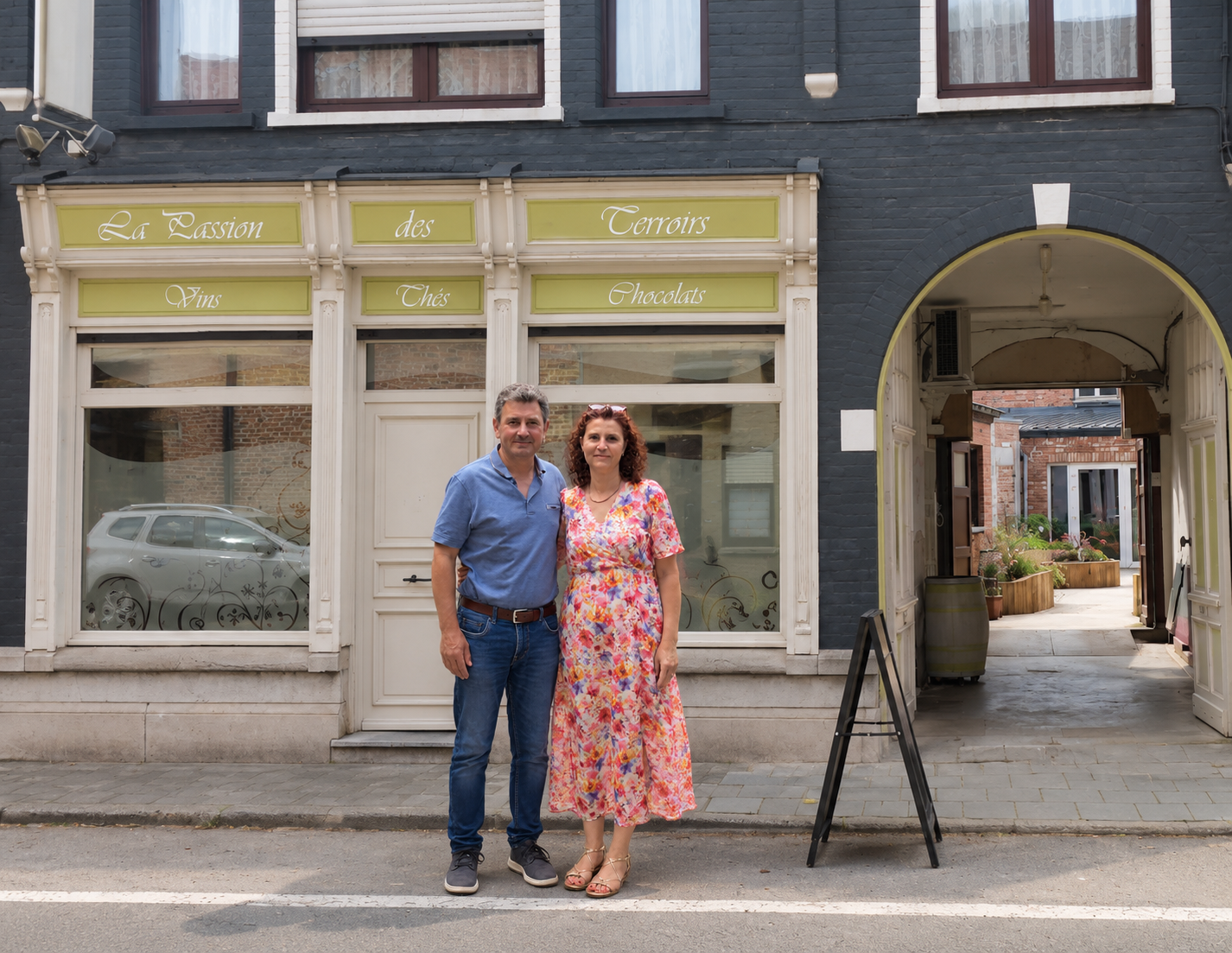 Matteo Russo et son épouse devant La Passion des Terroirs à Comines : devanture claire et enseigne « Vins, Thés, Chocolats », porche ouvert sur la cour